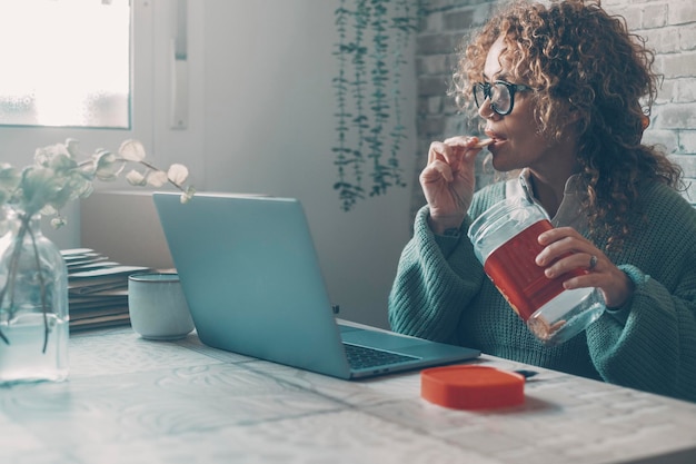 Una donna a casa che usa il computer portatile e mangia i biscotti dalla scatola Concetto di cattiva alimentazione abitudini alimentari stile di vita persone di sesso femminile e attività lavorativa sedentaria Signora carina godersi il tempo a casa da sola navigando sul web