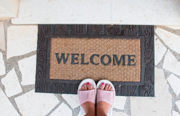 Una donna a piedi nudi in piedi davanti alla porta o una nuova casa con un tappeto di benvenuto, per favore good