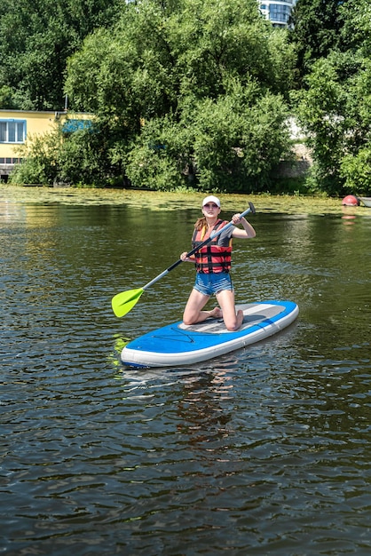 Una donna abbastanza snella galleggia su una tavola da sup e una lunga pagaia sul lago cittadino