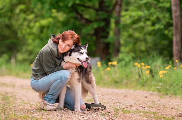 Una donna adulta abbraccia il suo soffice amico del Siberian Husky sulla strada sullo sfondo della foresta