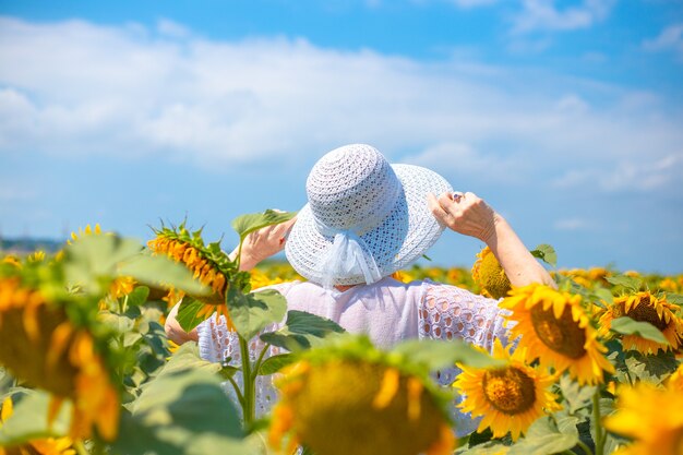 Una donna adulta con un cappello bianco si trova su un campo di girasoli