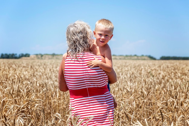 Una donna adulta con un ragazzo in braccio cammina in un campo di grano in una giornata di sole