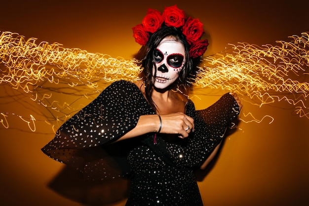 Una donna adulta con un trucco insolito per Halloween trascorre del tempo alla festa Modello con occhi scuri in top nero che guarda misteriosamente nella fotocamera