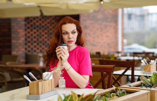 Una donna adulta è seduta in un bar estivo con una tazza di caffè e sorridente