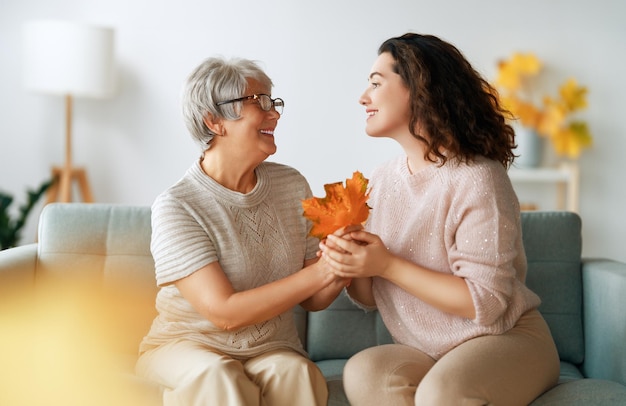 Una donna adulta felice e sua madre anziana con le foglie d'autunno all'interno