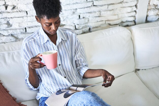 Una donna africana gioiosa si gode un caffè e una rivista nella sua giornata.