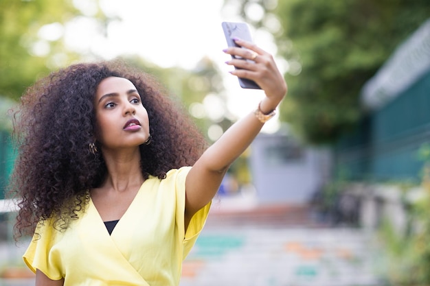 Una donna afro seria e sicura di sé con i capelli ricci che si fa un selfie durante il tramonto include spazio per la copia e il testo