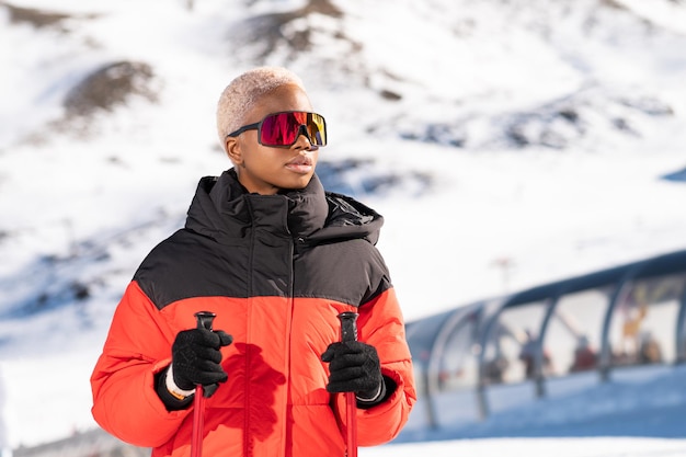 Una donna afroamericana con bastoncini da sci in piedi su una montagna innevata durante l'inverno