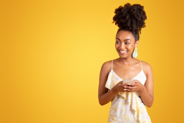 Una donna afroamericana sorridente che scrive su uno smartphone guardando uno spazio vuoto