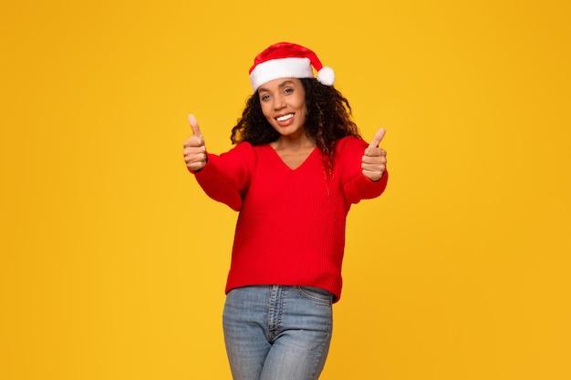 Una donna afroamericana sorridente con il cappello di Babbo Natale alza il pollice.