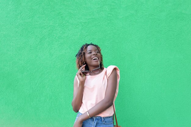 Una donna afroamericana sorridente con occhiali da sole in mano su uno sfondo verde Copia spazio