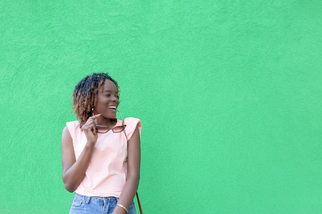 Una donna afroamericana sorridente con occhiali da sole in mano su uno sfondo verde Copia spazio