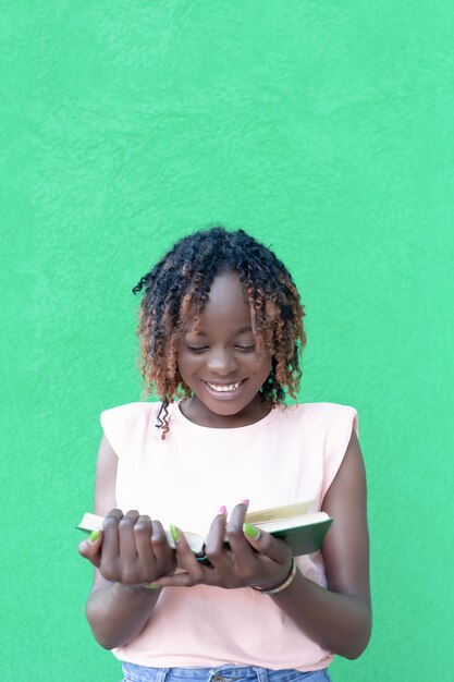 Una donna afroamericana sorridente su sfondo verde legge un libro Emozioni positive Ritorno a scuola