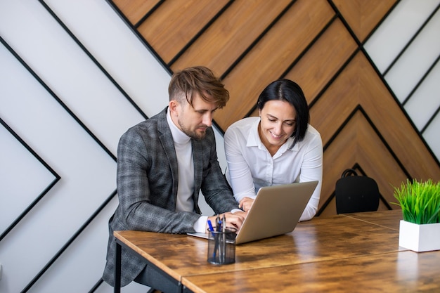 Una donna aiuta un uomo a lavorare su un laptop in ufficio