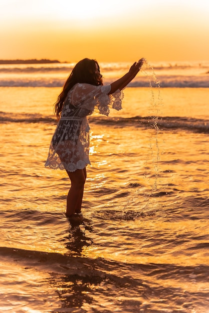 Una donna al tramonto in un vestito bianco che si gode l'acqua di mare in estate