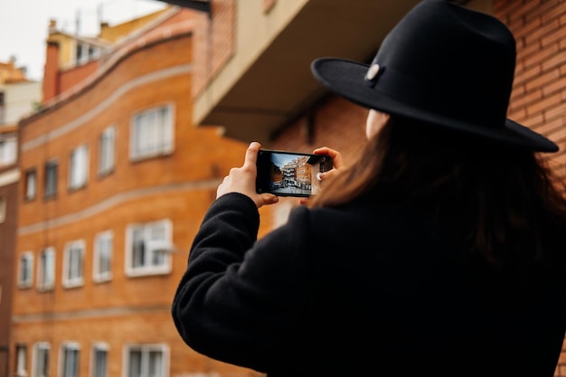 Una donna alla moda che indossa un cappello sta scattando una foto mentre cammina come turista
