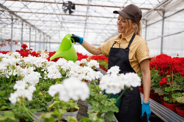 Una donna allegra, che lavora in un vivaio, innaffiando fiori da un serbatoio