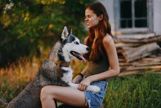 Una donna allegra con un cane di razza husky sorride mentre è seduta nella natura durante una passeggiata con un cane al guinzaglio paesaggio autunnale sullo sfondo Stile di vita nelle passeggiate con gli animali domestici