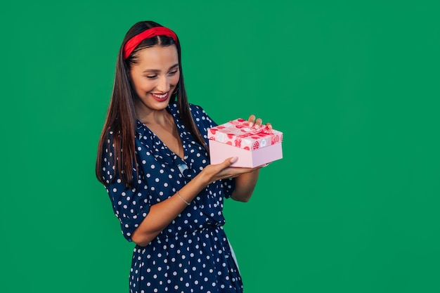 Una donna allegra con un vestito tiene in mano una confezione regalo e la apre per guardarci dentro