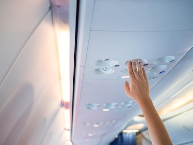 Una donna alza la mano per regolare il pannello della console del condizionatore d'aria sopra il sedile dell'aereo