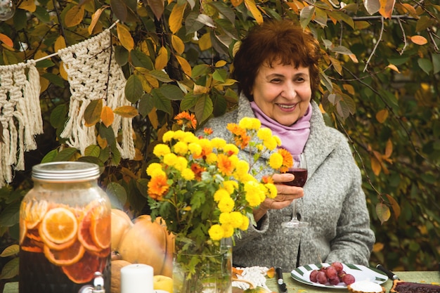 Una donna anziana ad un festoso tavolo autunnale della famiglia sorride felicemente.