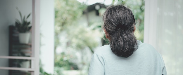 Una donna anziana anziana triste che guarda attraverso una finestra