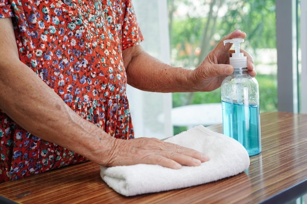 Una donna anziana asiatica preme un gel disinfettante alcolico blu per lavarsi le mani per proteggere dall'infezione da coronavirus