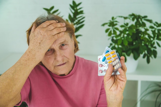 Una donna anziana beve una pillola per il mal di testa Messa a fuoco selettiva