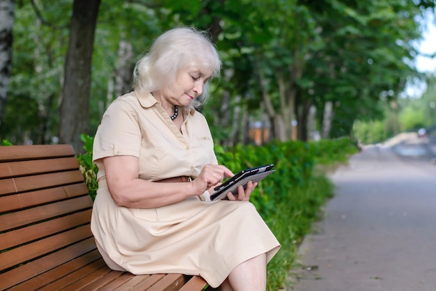 Una donna anziana con computer tablet nel parco