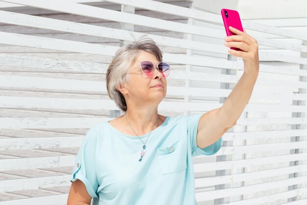 Una donna anziana con occhiali da sole colorati e una maglietta blu si fa un selfie