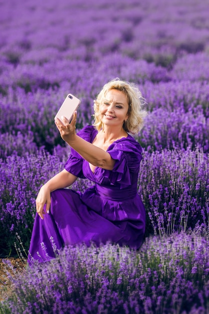 Una donna anziana con un telefono si fa un selfie in un campo di lavanda