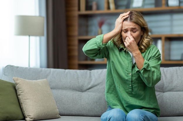 Una donna anziana è seduta a casa sul divano malata di influenza un raffreddore si pulisce il naso con un