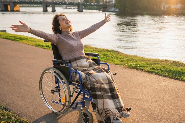 Una donna anziana felice in sedia a rotelle ha alzato le mani godendosi la libertà di camminare sulla strada nel parco della città all'aperto