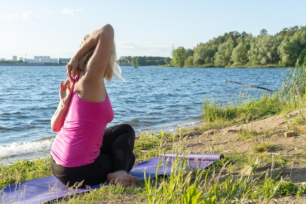 Una donna anziana in abiti sportivi che pratica yoga posa di mucca seduta e tenendo le mani piegate insieme