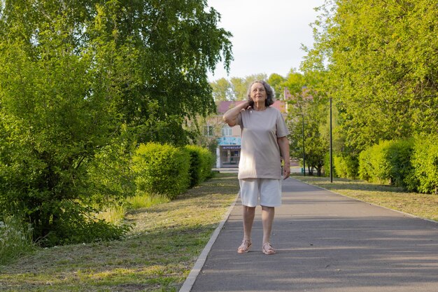 Una donna anziana in pantaloncini corti con i capelli grigi cammina attraverso il parco