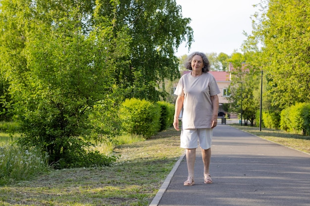 Una donna anziana in pantaloncini corti con i capelli grigi cammina attraverso il parco