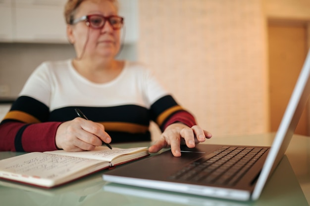 Una donna anziana in sovrappeso siede alla sua scrivania e studia attraverso il suo laptop