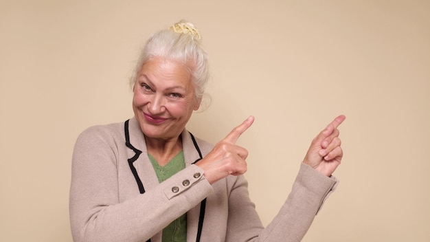 Una donna anziana punta il dito per attirare l'attenzione su uno sfondo beige