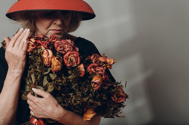 Una donna anziana sconvolta tiene un mazzo di fiori di rosa antica secca