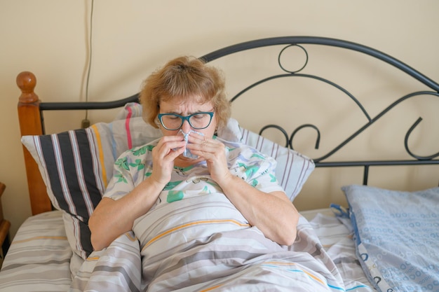 Una donna anziana soffre di influenza e naso che cola Il pensionato si soffia il naso nella zattera nasale