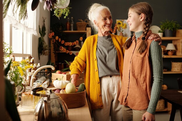 Una donna anziana sorridente che abbraccia la sua allegra nipote in cucina