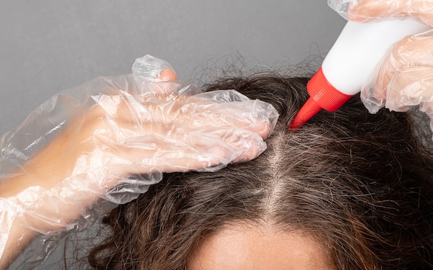 Una donna applica la tintura alle radici dei suoi capelli dipinge i capelli grigi grigi