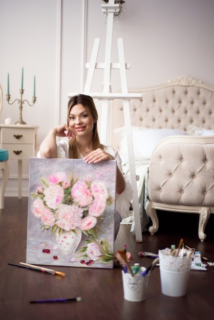 Una donna artista tiene una foto su un cavalletto a casa. Il pittore dipinge dipinti ad olio.
