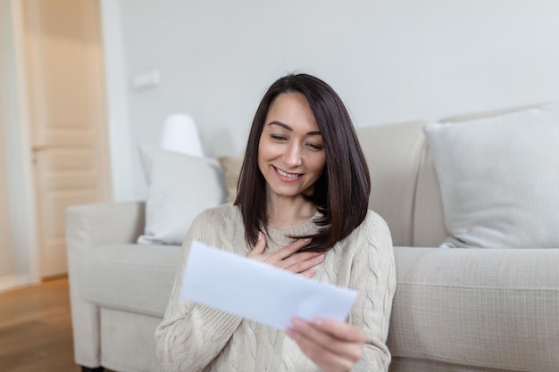 Una donna asiatica allegra preme la lettera ricevuta al petto a casa che riceve un invito o una buona notizia sull'assicurazione fiscale sui mutui ipotecari approvata che riceve avviso sull'accettazione della dichiarazione