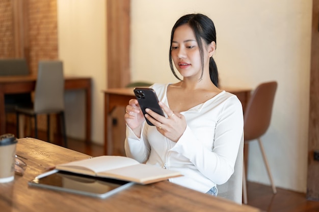 Una donna asiatica attraente usa il suo smartphone mentre si rilassa in un bar