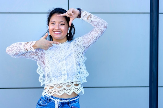 Una donna asiatica che ascolta musica con gli auricolari in strada con un muro grigio sullo sfondo