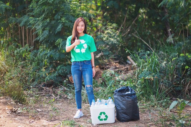 Una donna asiatica che fa il segno con la mano mentre raccoglie le bottiglie di plastica della spazzatura in un cestino all'aperto