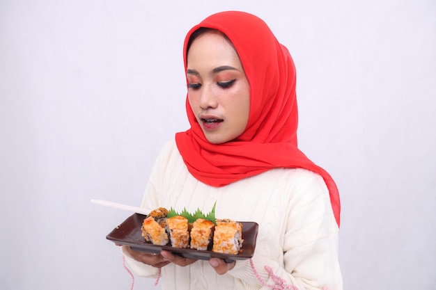 Una donna asiatica che indossa un hijab ha scioccato la candidata con entrambe le mani che tiene un piatto contenente sushi giapponese