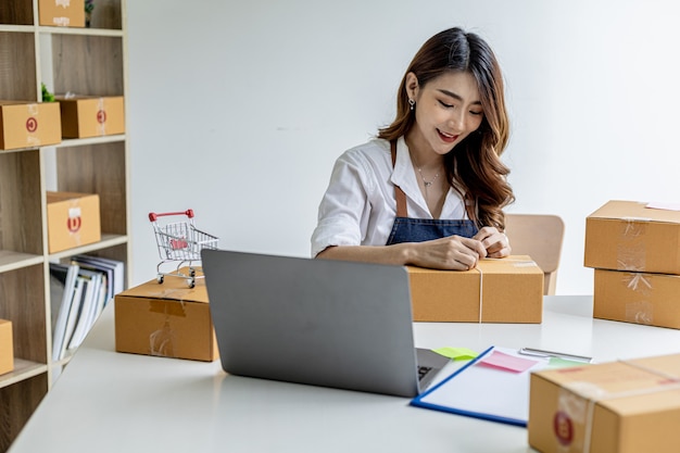 Una donna asiatica che lega un pacco alla scatola di un cliente, possiede un negozio online, imballa e spedisce tramite una compagnia di trasporti privata. Concetti di vendita online e shopping online.