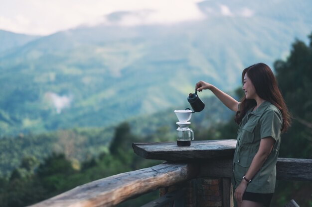 Una donna asiatica che prepara caffè a goccia con una bellissima montagna verde e la natura sullo sfondo